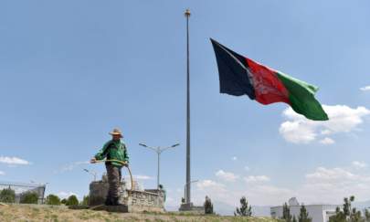 A worker waters a lawn near an Afghan national flag flying at half-mast in Kabul on May 11, 2021 during a national day of mourning announced by Afghan President Ashraf Ghani to condemn the recent terrorist attacks. (Wakil Kohsar/AFP via Getty Images)