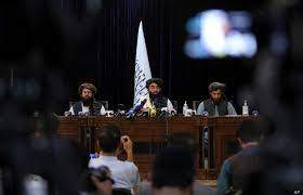 In front of a Taliban flag, Taliban spokesman Zabihullah Mujahid, center, speaks at his first news conference, in Kabul, Afghanistan, Aug. 17, 2021. K